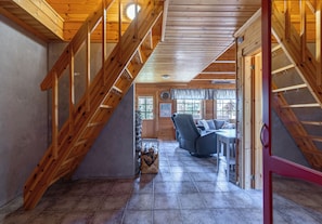 Un intĂ©rieur en bois avec un escalier, un espace de vie comprenant un canapĂ© et une table, ainsi quâune cheminĂ©e.