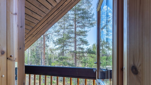 A wooden deck with a railing, a view of a forest, and a clear sky.