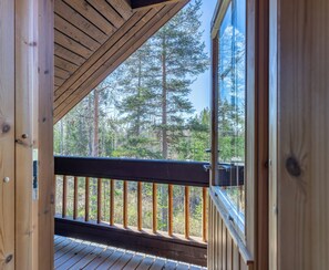 Una terraza de madera con barandilla, vista a un bosque y cielo despejado.