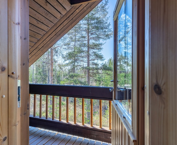 Une terrasse en bois avec une rambarde, une vue sur une forĂȘt et un ciel dĂ©gagĂ©.