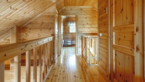 A wooden interior with a sloped ceiling, a central hallway, and wooden walls.