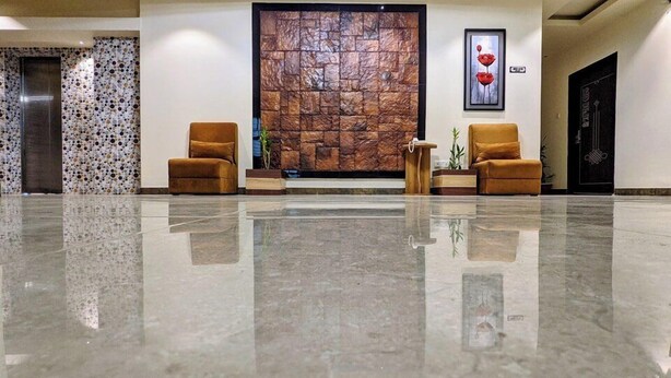 Un vestíbulo con piso pulido, dos sillones, una mesita de madera, un gran muro de piedra y una obra de arte enmarcada.