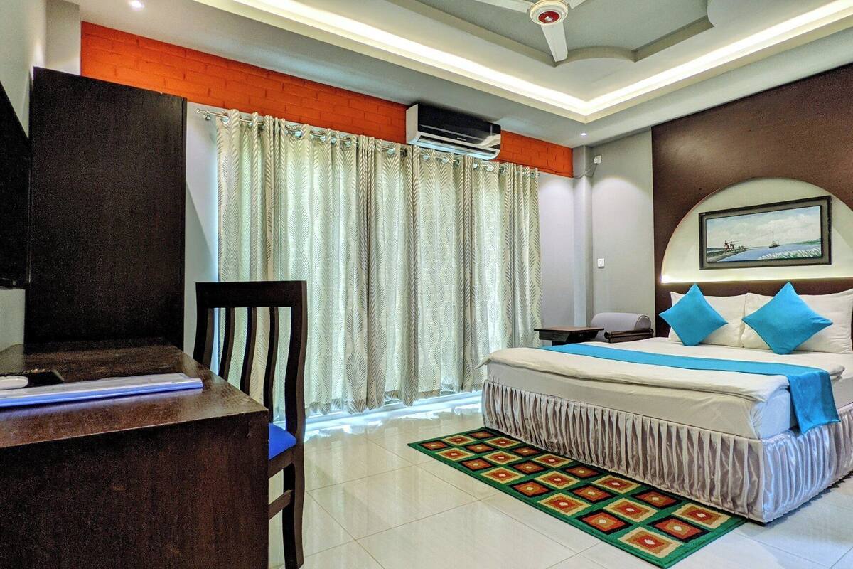 Habitación de hotel con cama, escritorio, silla, televisor y ventana con cortinas.