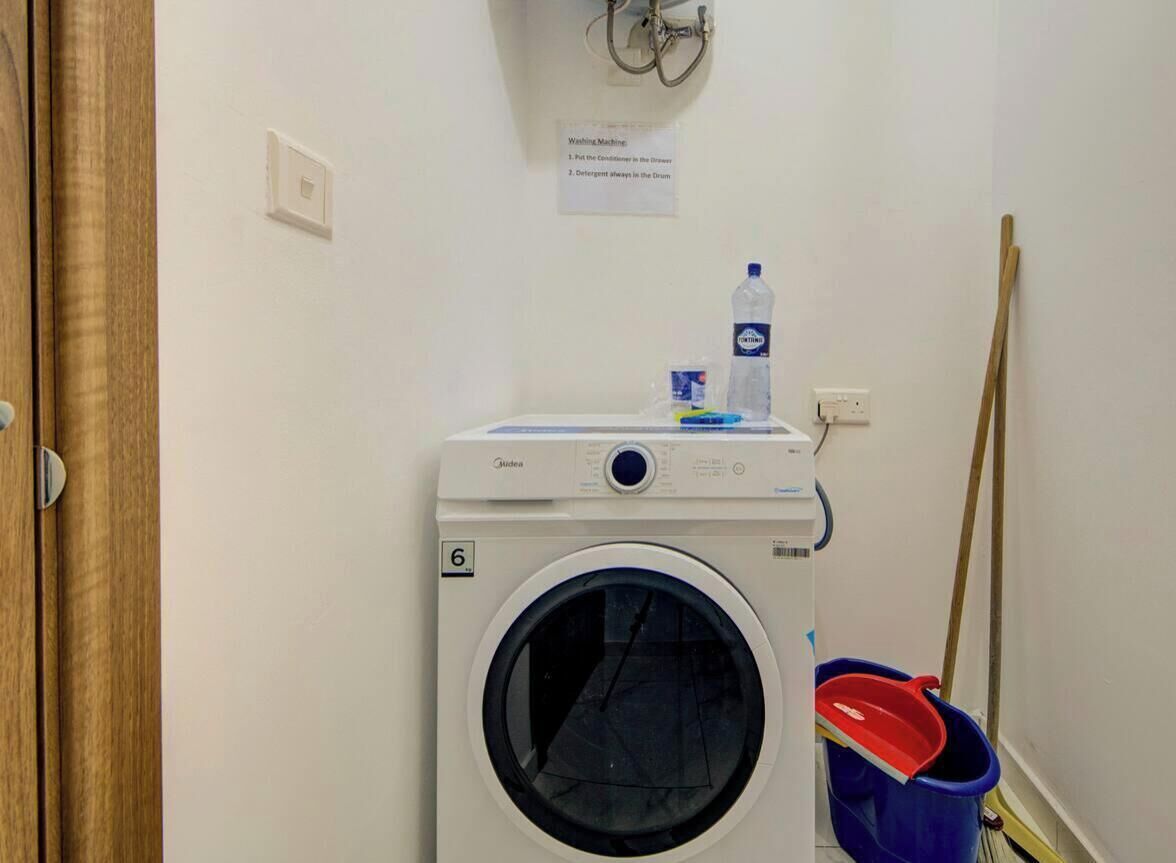 A washing machine in a laundry room with a sign above it, a mop, and a bucket.