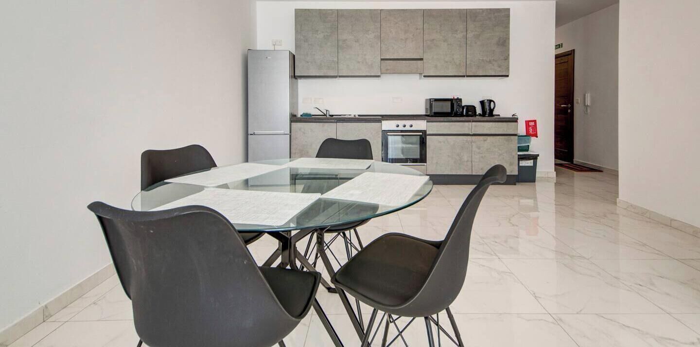 A modern kitchen with a dining area, including a glass table and black chairs.
