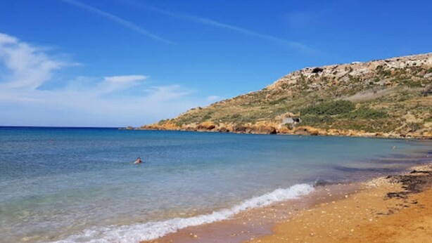 Una spiaggia con acque cristalline, una riva sabbiosa e una collina rocciosa sullo sfondo.
