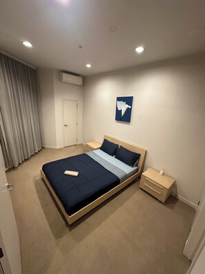Ein Schlafzimmer mit Bett, Nachttischen, einer Wand-Klimaanlage und einem Gemälde.