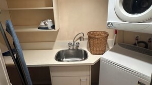 Un área de lavandería compacta con lavadora, un lavabo y una estantería con ropa doblada.