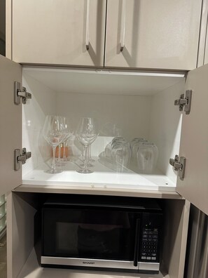 Eine Küche mit Mikrowelle und einem Schrank voller Weingläser.