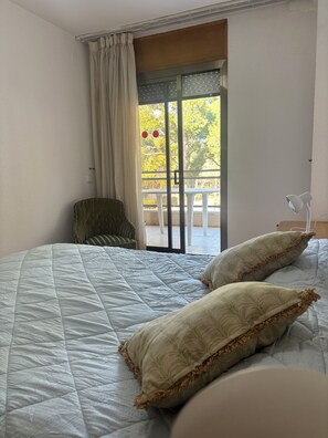 A bedroom with a bed, pillows, a chair, a lamp, and a view of an outdoor balcony. - In the heart of Salou, Senator Building (Salou)