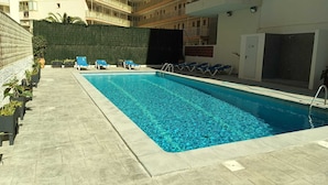 A swimming pool with lounge chairs, a tiled deck, and a high-rise building in the background. - In the heart of Salou, Senator Building (Salou)