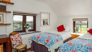 A bedroom with two beds, a chair, a desk, a window with a view, and a mirror. - Trehaverock Cottage (Port Isaac)