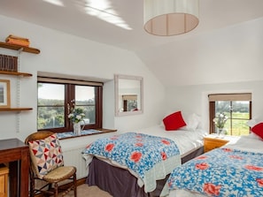 Ein Schlafzimmer mit zwei Betten, einem Sessel, einem Schreibtisch, einem Fenster mit Ausblick und einem Spiegel.