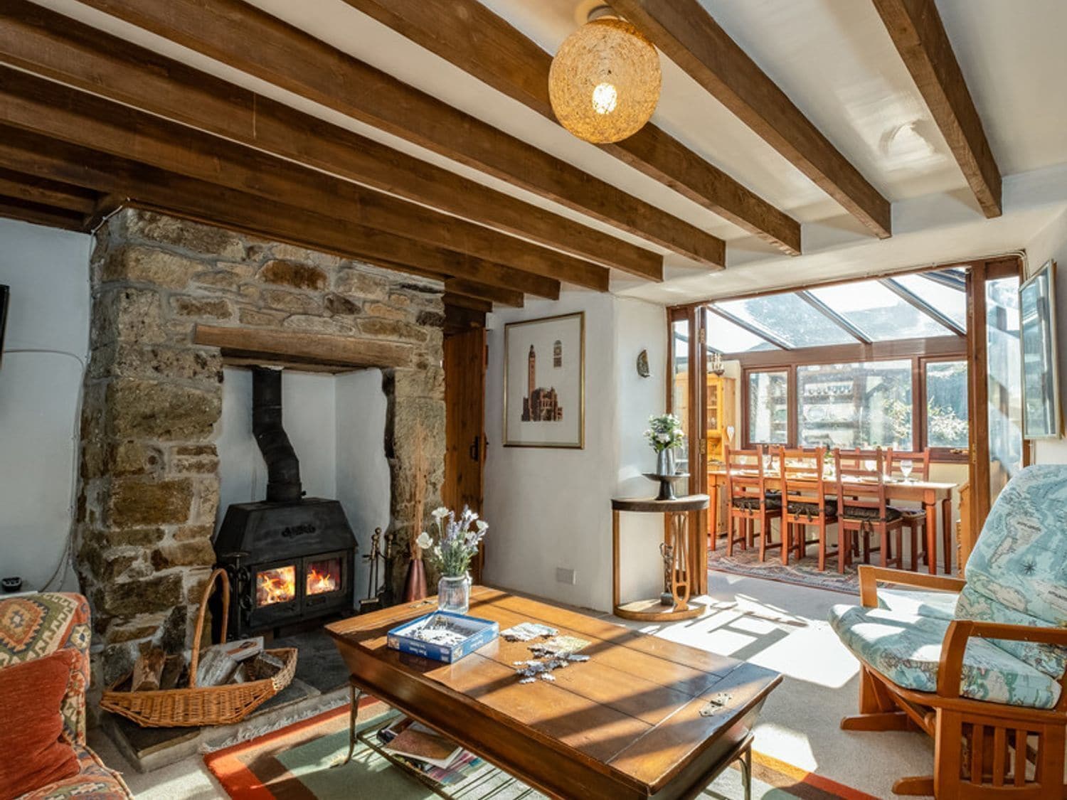 Una sala de estar acogedora con chimenea de piedra, vigas de madera, comedor con mesa y sillas, y un ventanal con vistas.