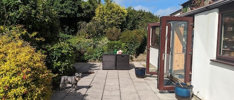 Eine gepflasterte Terrasse mit Sitzgelegenheit, einem kleinen Tisch mit Teekanne und einer hölzernen Bank.