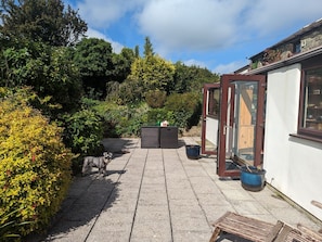 Eine gepflasterte Terrasse mit Sitzgelegenheit, einem kleinen Tisch mit Teekanne und einer hölzernen Bank.