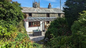 A stone house with a conservatory, surrounded by lush greenery. - Trehaverock Cottage (Port Isaac)