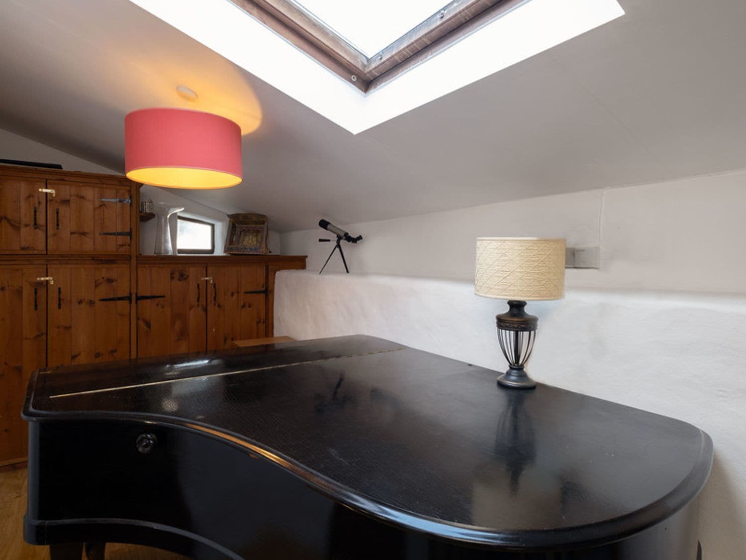 Una habitación con tragaluz, una mesa negra, armarios de madera, un telescopio y una lámpara.