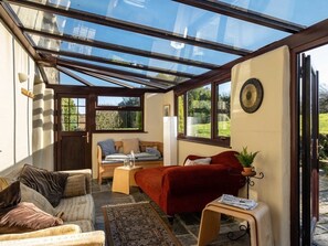 Ein sonnendurchfluteter Raum mit Glasdecke, einem roten Sofa, einer Holzbank und einem kleinen Tisch mit Pflanze.