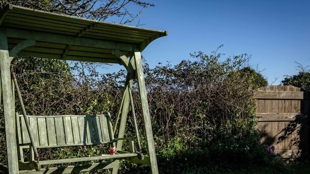 A wooden swing set in a garden with a wooden fence and dense foliage in the background. - Trehaverock Cottage (Port Isaac)