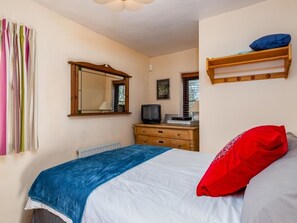 Une chambre à coucher comprenant un lit, une commode, un téléviseur, un miroir et une fenêtre avec des stores.