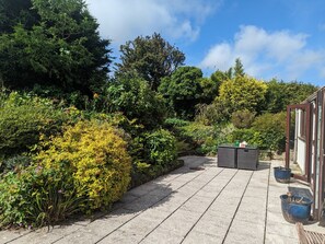 Un chemin pavé mène à un bâtiment doté d’une porte en verre, qui est entouré d’une végétation luxuriante et de diverses plantes.