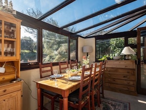 A dining area with a wooden table set for four, surrounded by chairs, with a glass ceiling and windows offering a view of the outdoors. - Trehaverock Cottage (Port Isaac)