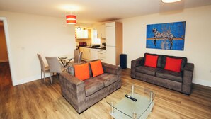 A living room with two sofas, a glass coffee table, and a dining area with a chair and table.