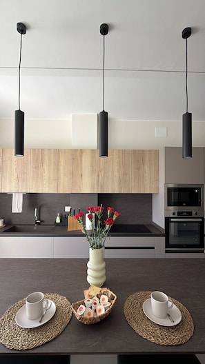 Uma cozinha moderna com luminárias pendentes, uma ilha central com um vaso de flores e um forno embutido.