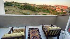 Un balcón con dos sillas de madera y un tapete estampado, con vistas a una zona residencial con casas y vegetación.