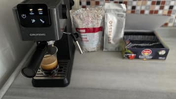 En kaffemaskine med digitalt display, en kop kaffe og poser med kaffebønner.
