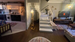 Una sala de estar moderna con una escalera, una cocina al fondo y un televisor mostrando el logotipo de Netflix.