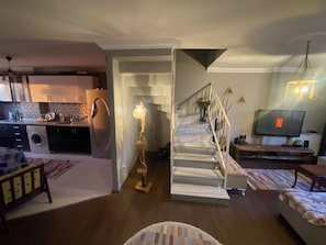 A modern living room with a staircase, a kitchen in the background, and a television displaying the Netflix logo.