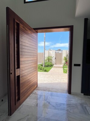 Una puerta de madera abierta que da a un espacio exterior empedrado bajo un cielo despejado.