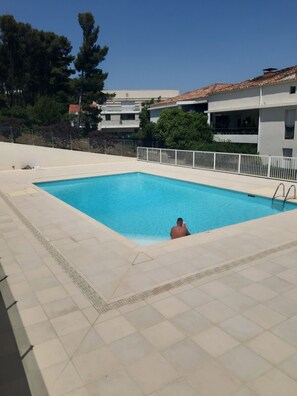 Ein rechteckiger Swimmingpool mit weiß gefliestem Beckenrand, einer Metallleiter und einer Person im Wasser.