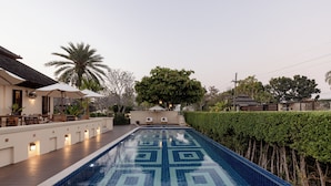 A swimming pool with a geometric tile pattern, surrounded by a wooden deck and a hedge. - Serene Maerim Villa (Mae Rim)