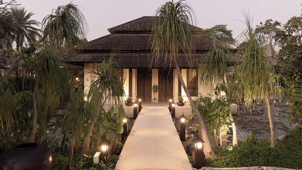 A building with a thatched roof, a pathway leading to the entrance, and potted plants along the sides. - Serene Maerim Villa (Mae Rim)