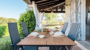 Uma área de refeições ao ar livre com mesa e cadeiras de madeira, e vista para o jardim.