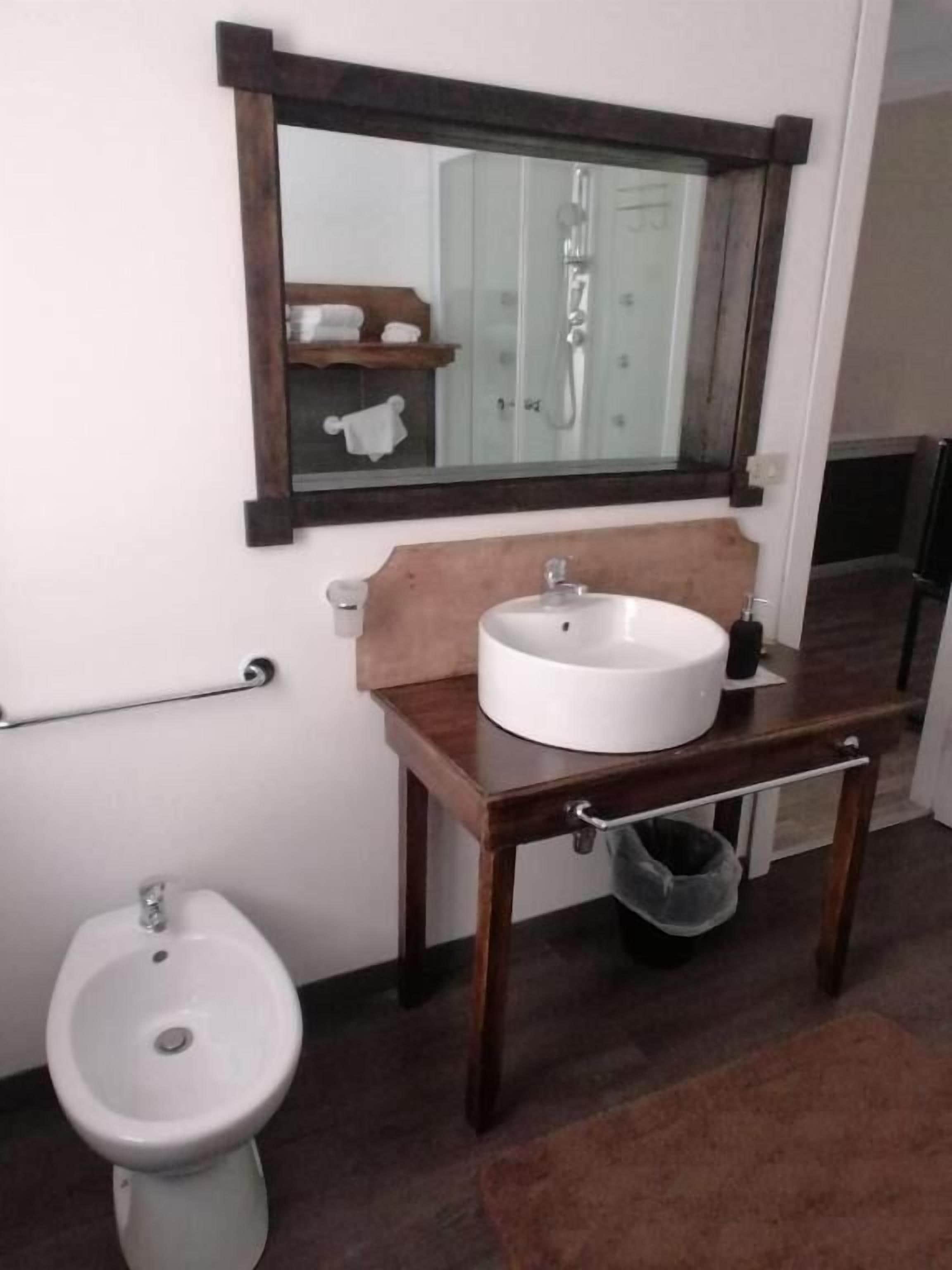 Un baño con tocador de madera, lavabo redondo, espejo, bidé y toallero.