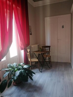 Una habitación con una mesa de comedor, sillas, una planta en maceta, un radiador y una puerta con la letra 'S'.