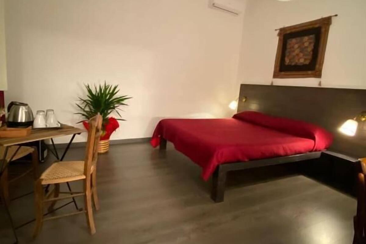 Ein Zimmer mit einem Bett, einem Schreibtisch, einem Sessel, einem Blumentopf und einer Wandleuchte.