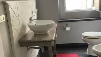 A bathroom with a white sink, a mirror, a toilet, and a window.