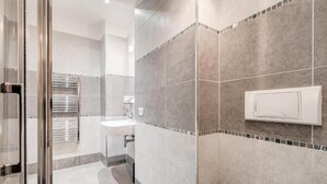 Een moderne badkamer met een douchecabine van glas, een witte wastafel en een betegelde douche.