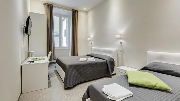 Een hotelkamer met twee bedden, een bureau, een televisie en een raam met gordijnen.