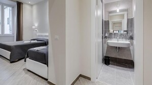Een moderne hotelkamer met twee bedden, een badkamer met wastafel en spiegel, en een raam met gordijnen.