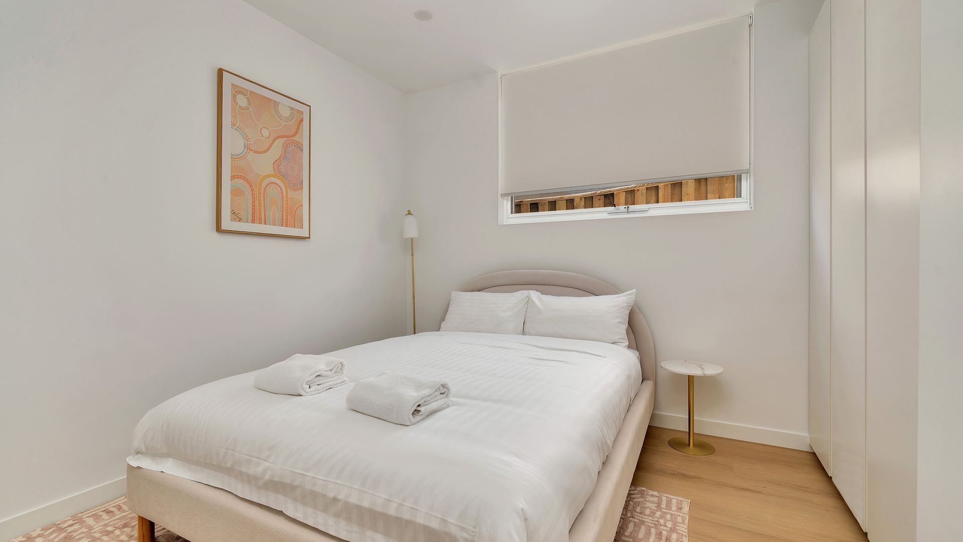 A bedroom with a bed, a bedside lamp, a window, and a painting on the wall.