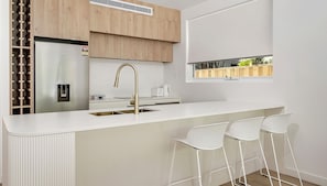 A modern kitchen with a central island, stainless steel appliances, and a window with a view. - Orion Garden Villa by Experience Jervis Bay (Vincentia)