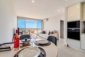A modern kitchen with built-in appliances, a dining area with a table set for two, and a view of the city through large windows. - [Algarve] - T1 Três Castelos (Portimão)