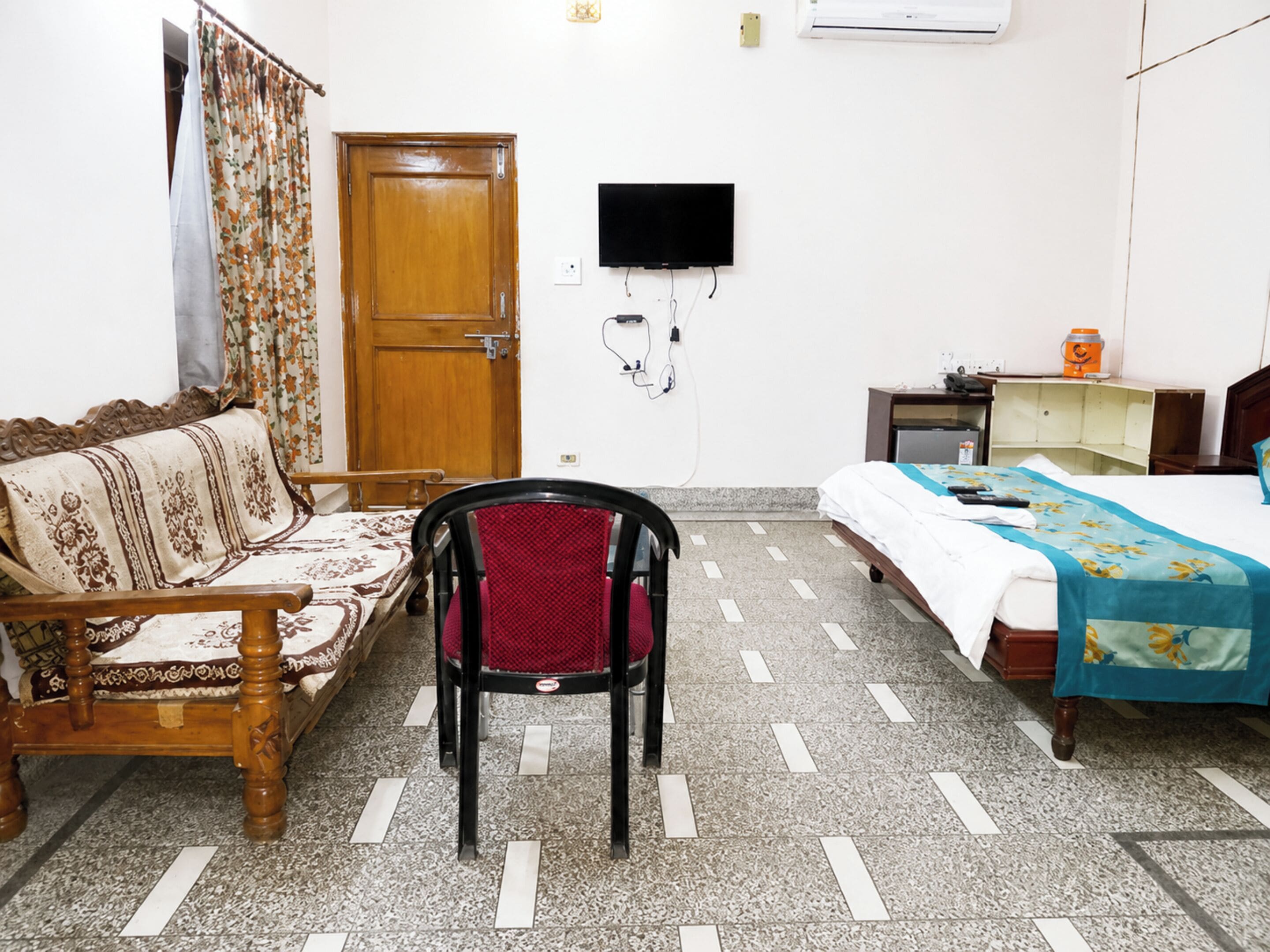 A room with a wooden bed, a wooden sofa, a red chair, a television mounted on the wall, and a tiled floor.