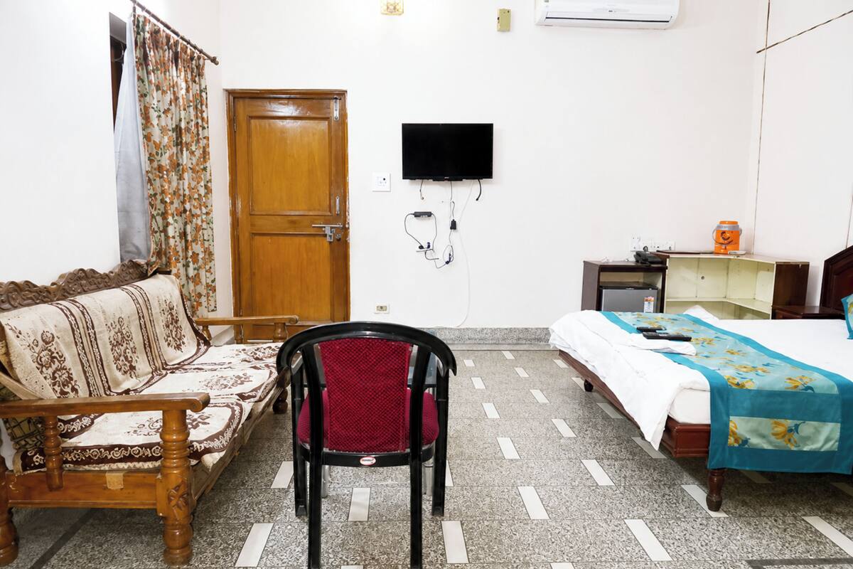 A room with a wooden bed, a wooden sofa, a red chair, a television mounted on the wall, and a tiled floor.